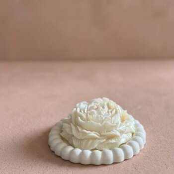 Vela artesanal Peonía con forma de flor blanca sobre un plato decorativo redondo de yeso.