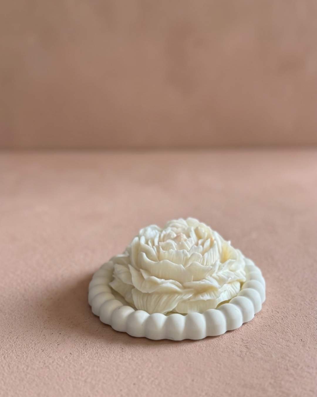 Vela artesanal Peonía con forma de flor blanca sobre un plato decorativo redondo de yeso.