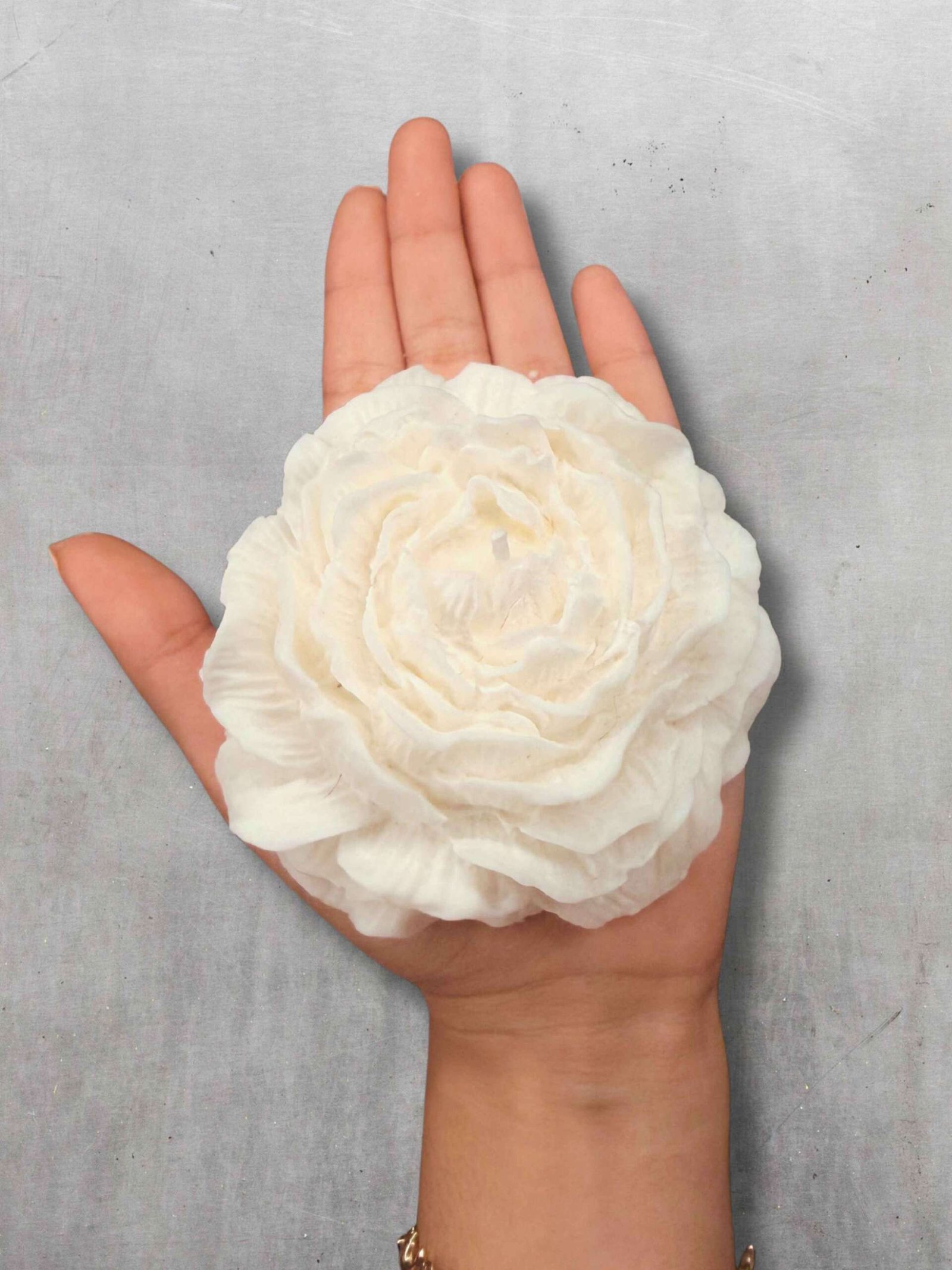 Vela artesanal Peonía con forma de flor blanca sobre un plato decorativo redondo de yeso.